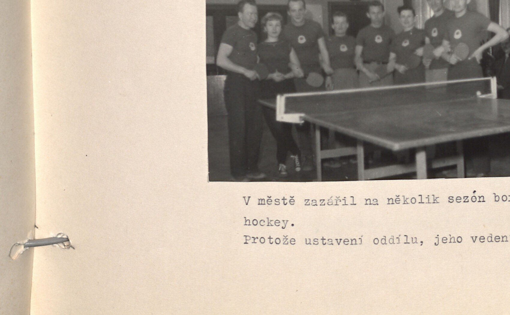 Černobílá fotografie: zápas / scéna ze stolního tenisu — hráči s pálkami u stolu na stolní tenis, kolem diváci.