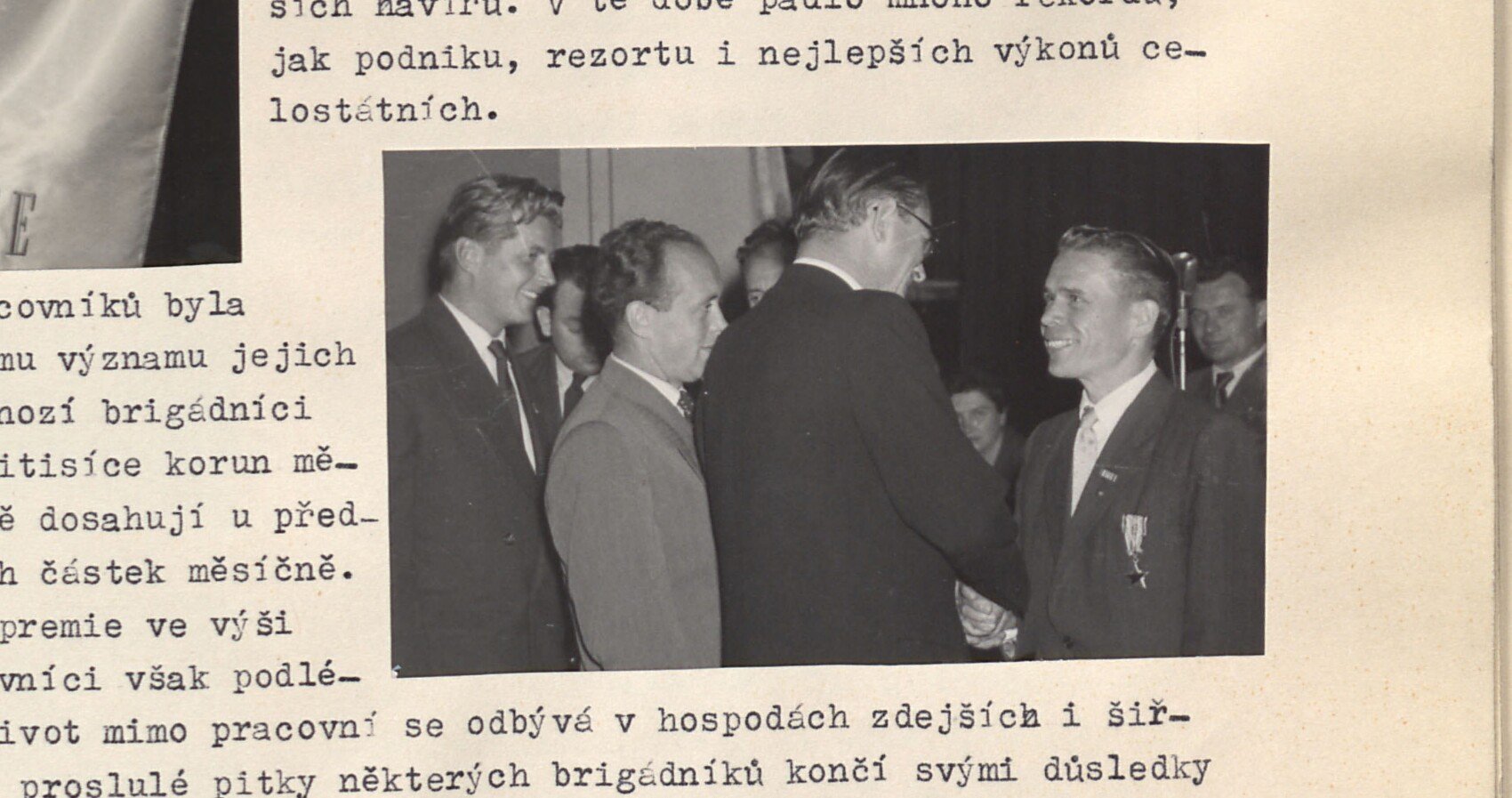Černobílá fotografie: slavnostní předávání vyznamenání — muži v oblecích, jednomu je připínáno/předáváno státní vyznamenání. Bez tištěné popisky.