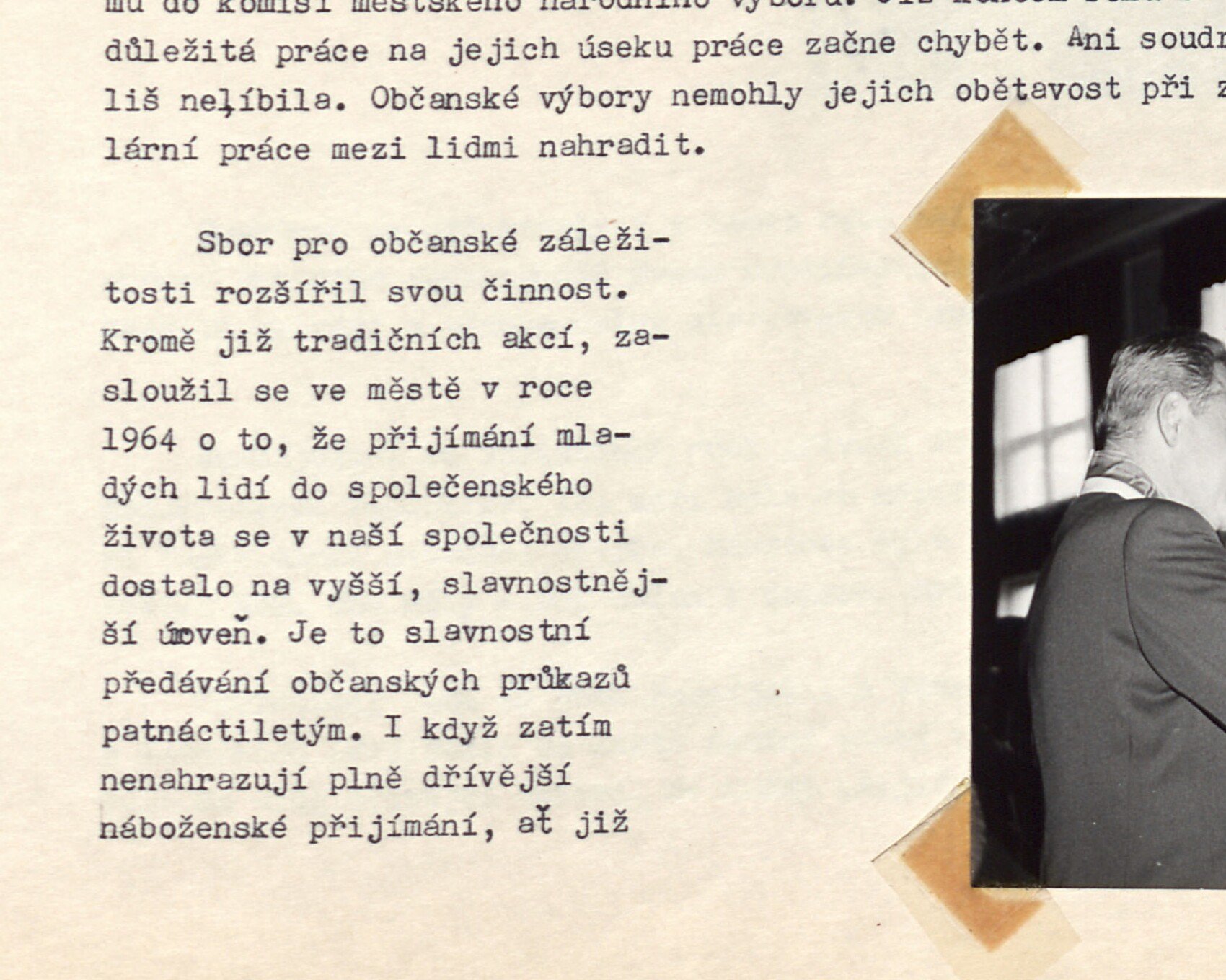 Slavnostní předávání občanských průkazů patnáctiletým – muž (funkcionář) předává průkaz mladé dívce; v pozadí okna sálu.