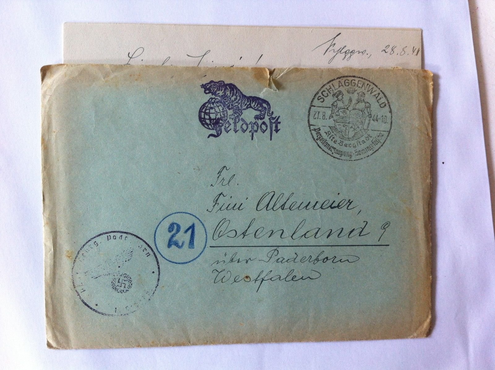 Feldpost obálka odeslaná ze Schlaggenwaldu (Horní Slavkov) adresovaná slečně Fini Altemeier do Ostenlandu u Paderbornu (Vestfálsko). Na obálce vytištěné logo polní pošty s tygrem sedícím na glóbu a nápisem „Feldpost", kruhové poštovní razítko „SCHLAGGENWALD 27.8.44" s městským znakem (dva horníci držící štít) a textem „Alte Bergstadt – Porzellanerzeugung – Sommerkurort" (Staré horní město – výroba porcelánu – letovisko). Vlevo dole cenzurní razítko s orlem a hákovým křížem (text nečitelný), vedle modře napsané číslo „21". Nad obálkou vykukuje vytažený dopisní list s ručně psaným úvodem a datem „…ggen., 28.8.44".
Text na snímku: SCHLAGGENWALD / 27.8. 44-10 / Alte Bergstadt / Porzellanerzeugung-Sommerkurort — Feldpost — Frl. Fini Altemeier, Ostenland 9, über Paderborn, Westfalen — [nečitelné razítko s orlem a hákovým křížem] — 21 — (na dopisním listu) L... [nečitelné] !  ...ggen., 28.8.44