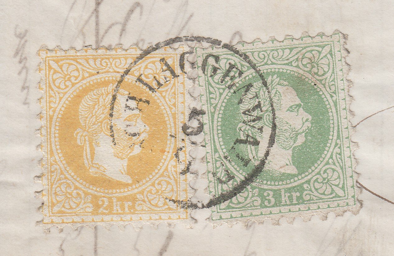 Detail poštovních známek na dopisní zásilce – rakouská emise s hlavou Františka Josefa I. (žlutá 2 kr. a zelená 3 kr.), přes ně otisk kulatého poštovního razítka s částečně čitelným textem „...GEN...WALD" (pravděpodobně Schlaggenwald, tj. Horní Slavkov) a číslicí „5" v datu. V pozadí rukopisná adresa perem.
