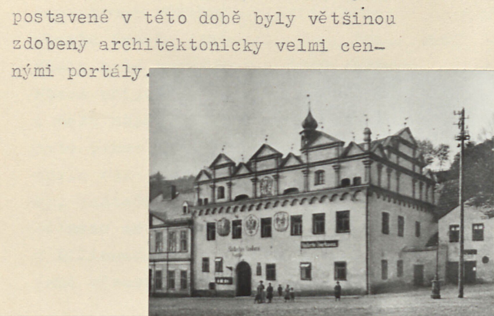 Černobílá fotografie historického domu na náměstí v Horním Slavkově – budova s renesančním štítem a dvěma malovanými znaky na fasádě (městský znak a český lev), v popředí náměstí.