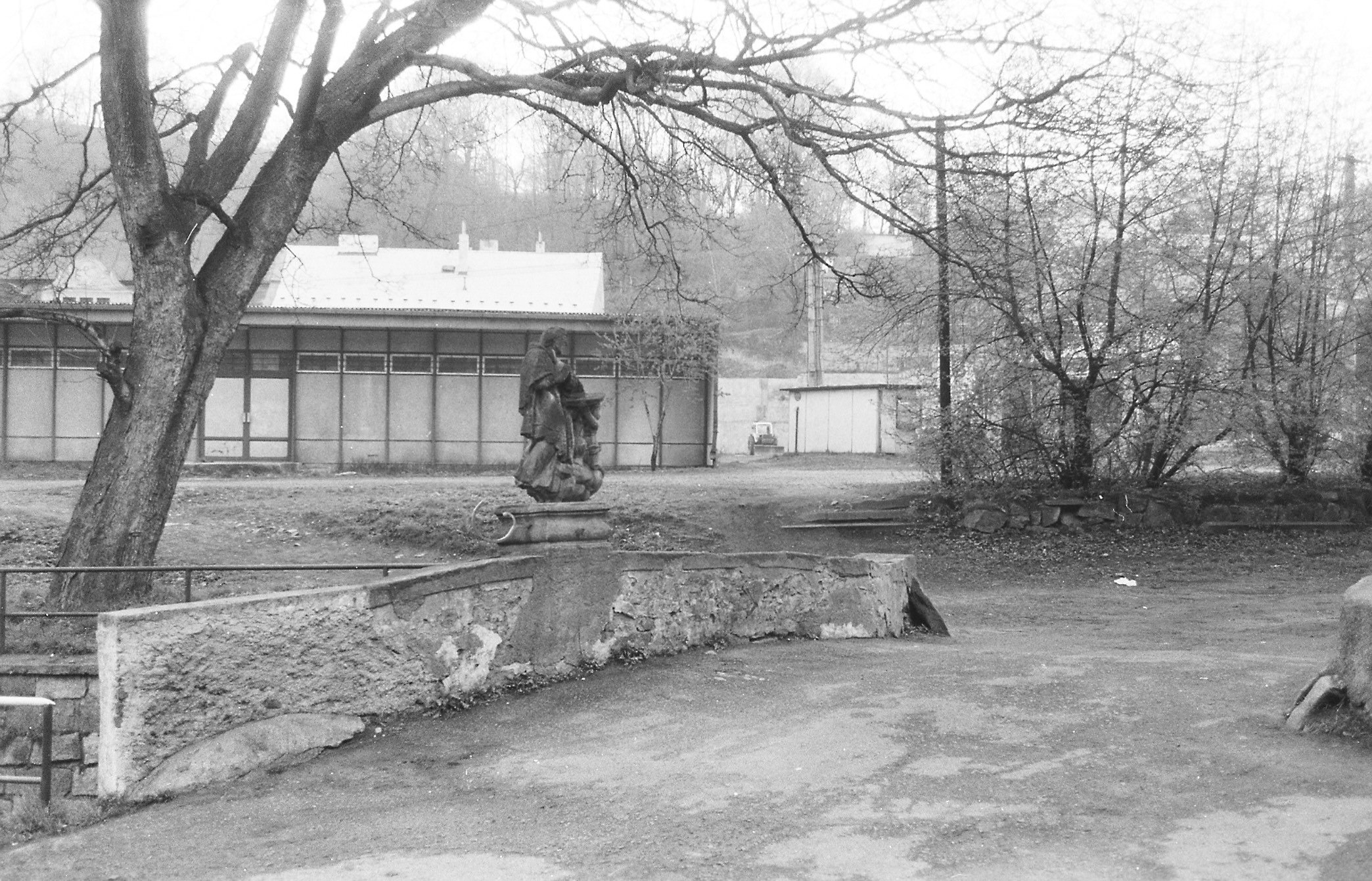 Sv. Jan Nepomucký. V pozadí betonový obchod, který nahradil původní historickou zástavbu
