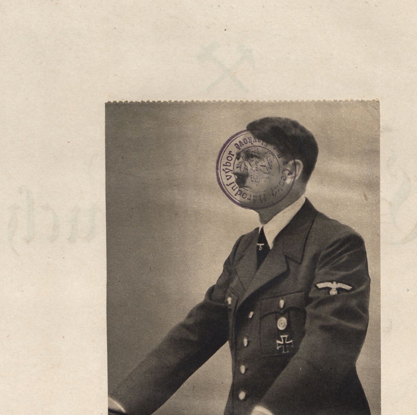 Nalepená dobová fotografie Adolfa Hitlera v uniformě, jak řeční (stojí u řečnického pultu). Přes obličej je otištěno fialové oválné razítko města Horní Slavkov. Tištěné popisky: „Aufn.: Hoffmann — Der Führer spricht im Reichstag" (Vůdce hovoří v říšském sněmu) a citát Adolfa Hitlera.