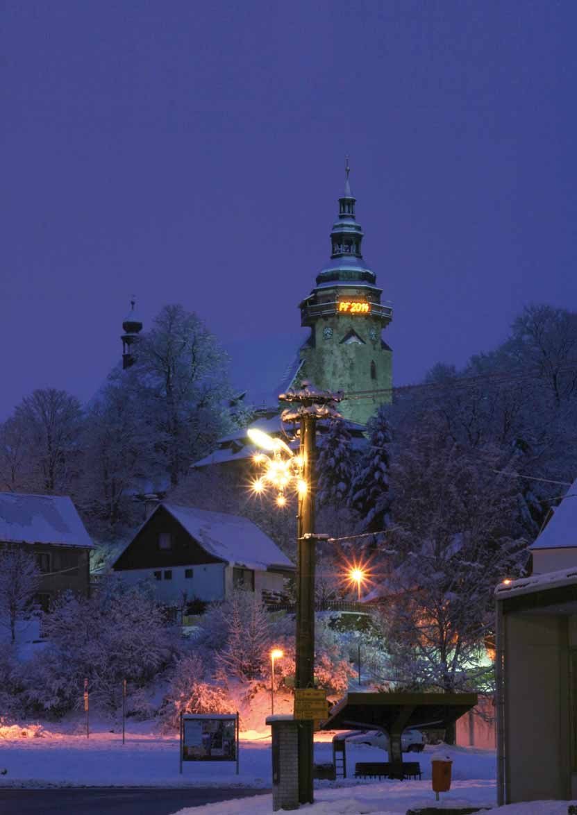 Zimní podvečerní pohled na město s rozsvíceným pouličním osvětlením a kostelní věží (Slavkovský zpravodaj, 1/2014)