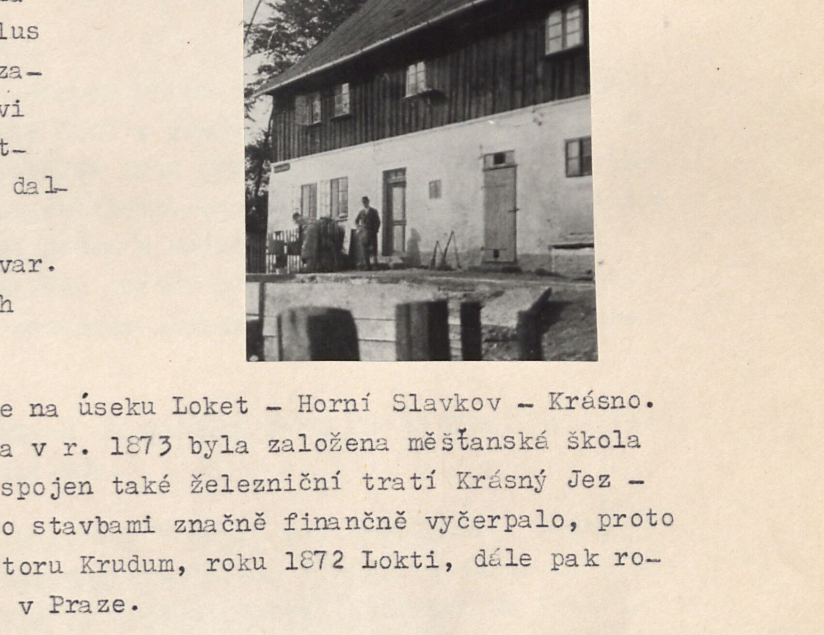 Velká patrová hrázděná budova (továrna na porcelán / zemědělská usedlost) se skupinkou osob před vstupem