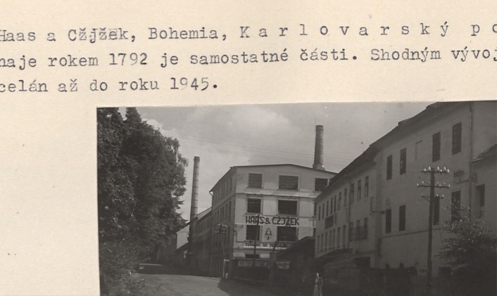 Budova porcelánky (Karlovarský porcelán) na hlavní ulici - pohled na tovární komín a fasádu s nápisem.