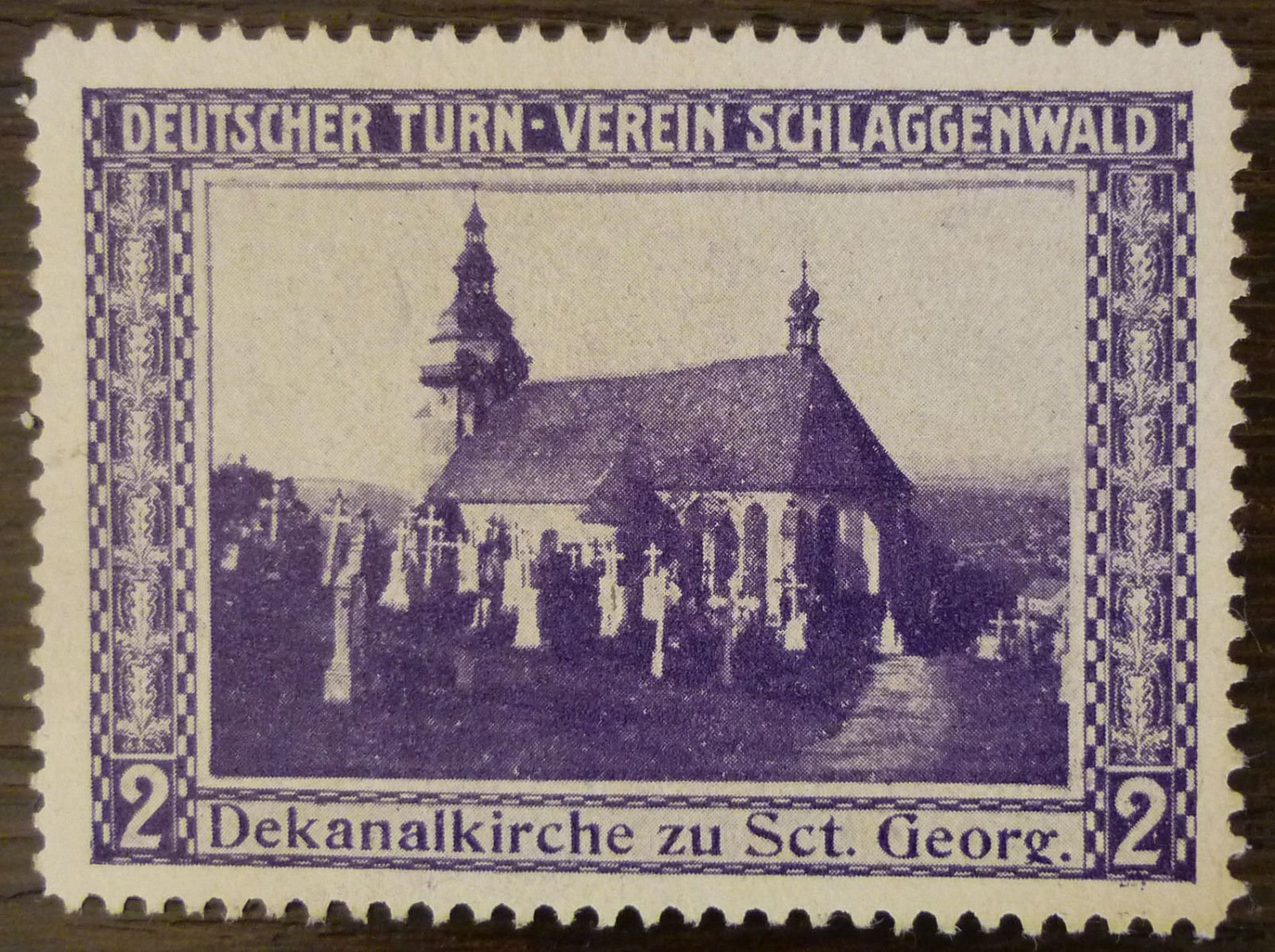 Dobová propagační/dobročinná známka spolku „Deutscher Turn-Verein Schlaggenwald" (Německý tělovýchovný spolek Slavkov) v hodnotě 2 (haléřů/feniků), s vyobrazením děkanského kostela sv. Jiří (Dekanalkirche zu Sct. Georg) obklopeného hřbitovem s kříži. Text na známce: „DEUTSCHER TURN-VEREIN SCHLAGGENWALD" a „Dekanalkirche zu Sct. Georg." s čísly hodnoty „2" po stranách.