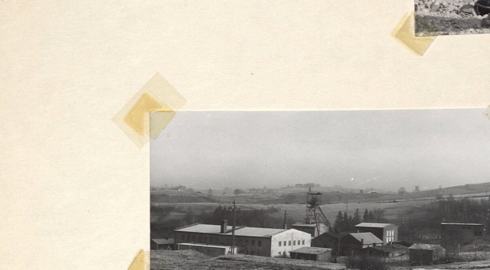 Černobílá fotografie krajiny s průmyslovými budovami a těžní věží šachty 3 v Horním Slavkově, v pozadí kopce.