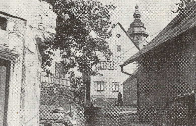 Pohled do úzké dlážděné uličky (Untere Kirchstaffel – Dolní kostelní schody) v Horním Slavkově, lemované starými kamennými a hrázděnými domy, v pozadí kostelní věž.