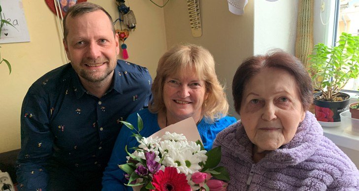 Gratulace k 85. narozeninám – oslavenkyně s rodinou a kyticí (Slavkovský zpravodaj, 3/2025)